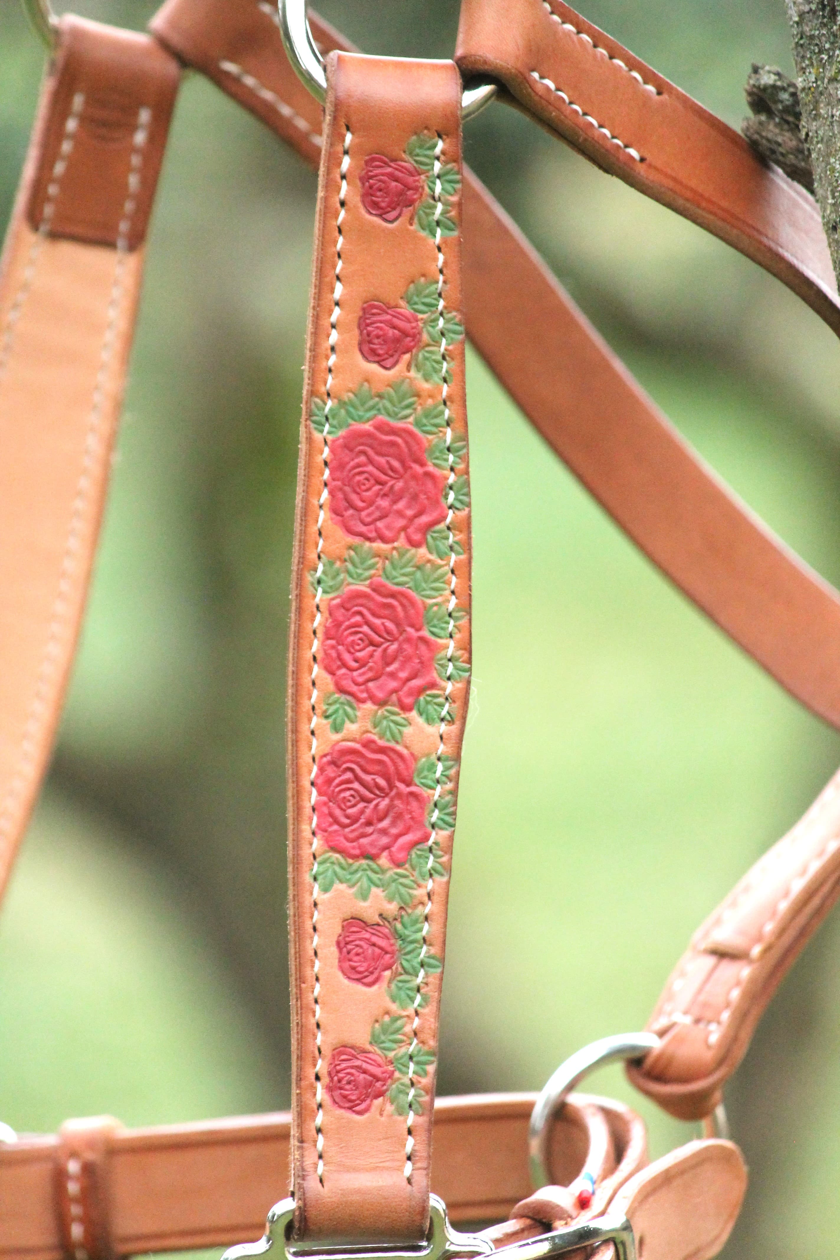 Détail macro d'une broderie de roses rouges sur cuir tan, fil de soie et cire à brûler.